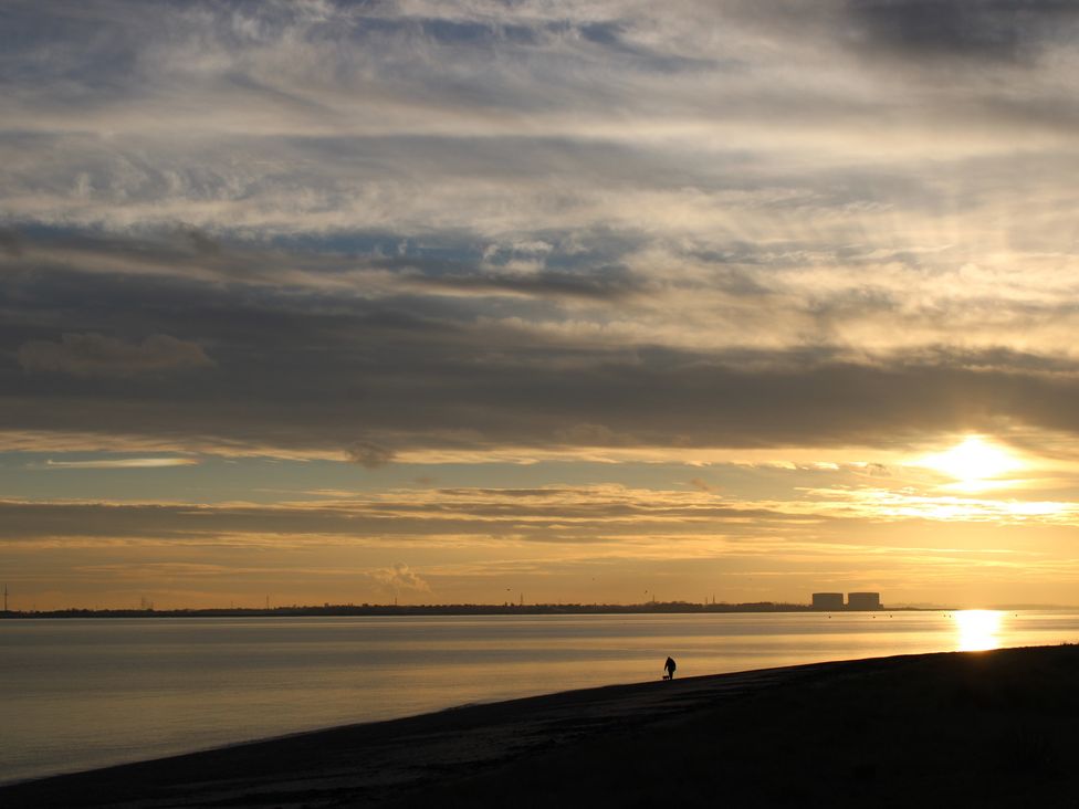 A sunset over water with a person walking along the shore at an unspecified location