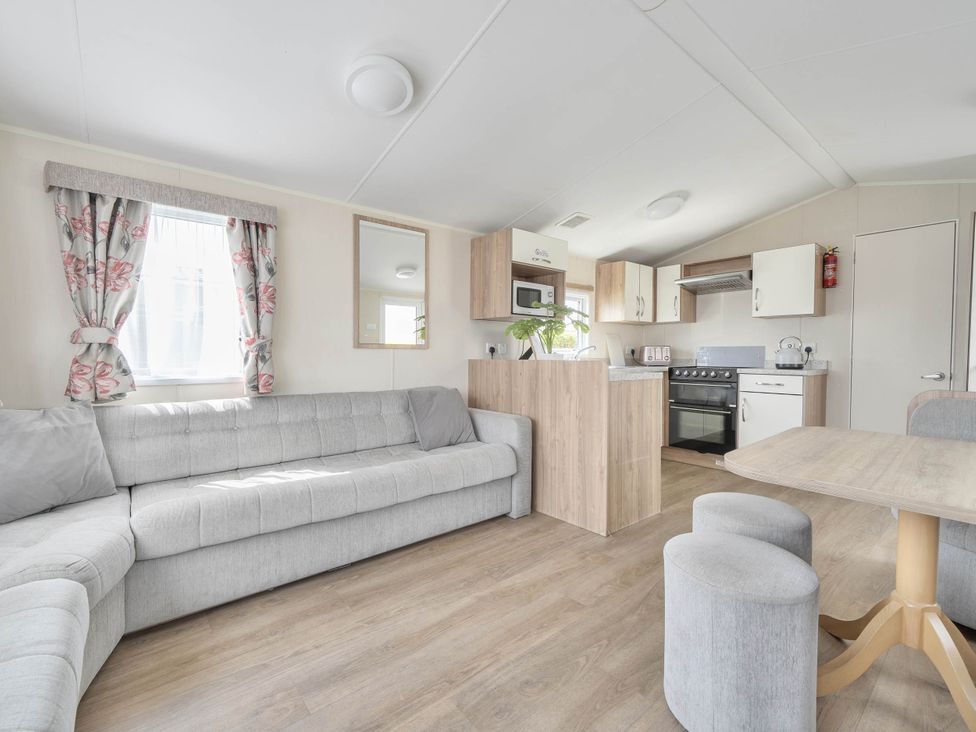 A living room with a sofa and kitchen area at Mersea Beach Retreat in Colchester
