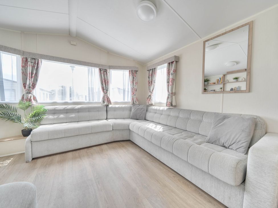 A living room with a sectional sofa and windows at Mersea Beach Retreat in Colchester