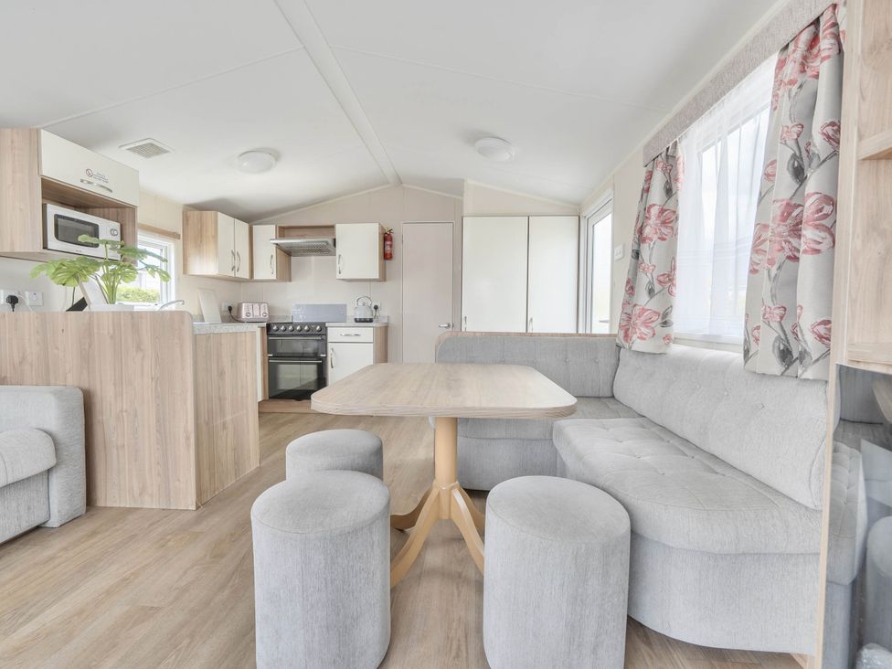 A living room with a sofa, table, and kitchen units at Mersea Beach Retreat in Colchester