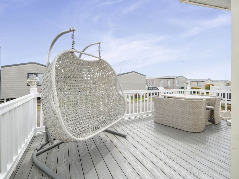 An outdoor terrace with a hanging chair and table at Mersea Beach Retreat in Colchester
