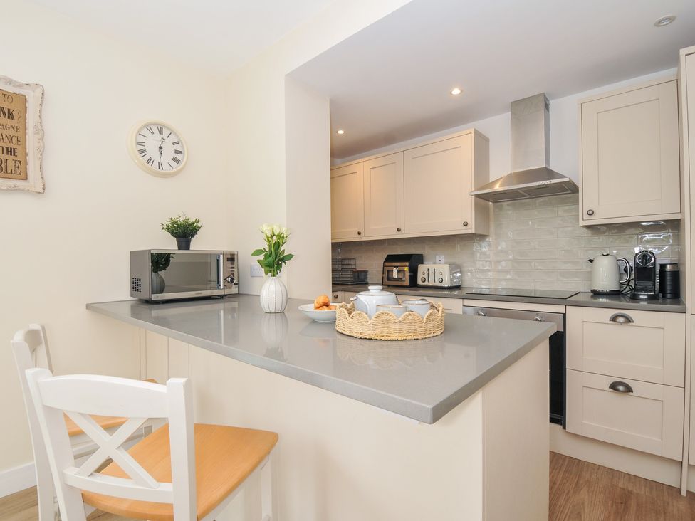 A kitchen with a microwave, kettle, and bar stools at Barton House in Looe