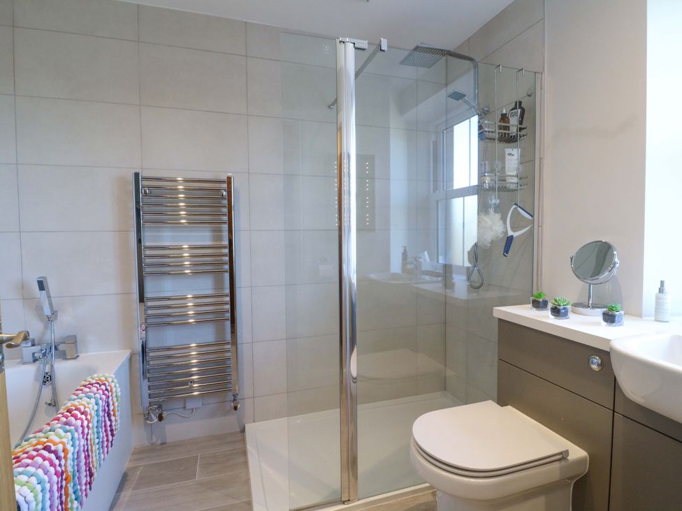 A bathroom with bathtub, shower, towel radiator, and sink at 7 Catcliffe Cottages Bakewell