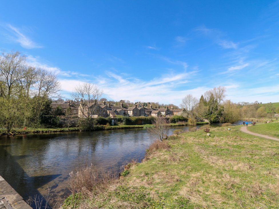 A view of a river alongside houses and trees at 7 Catcliffe Cottages in Bakewell