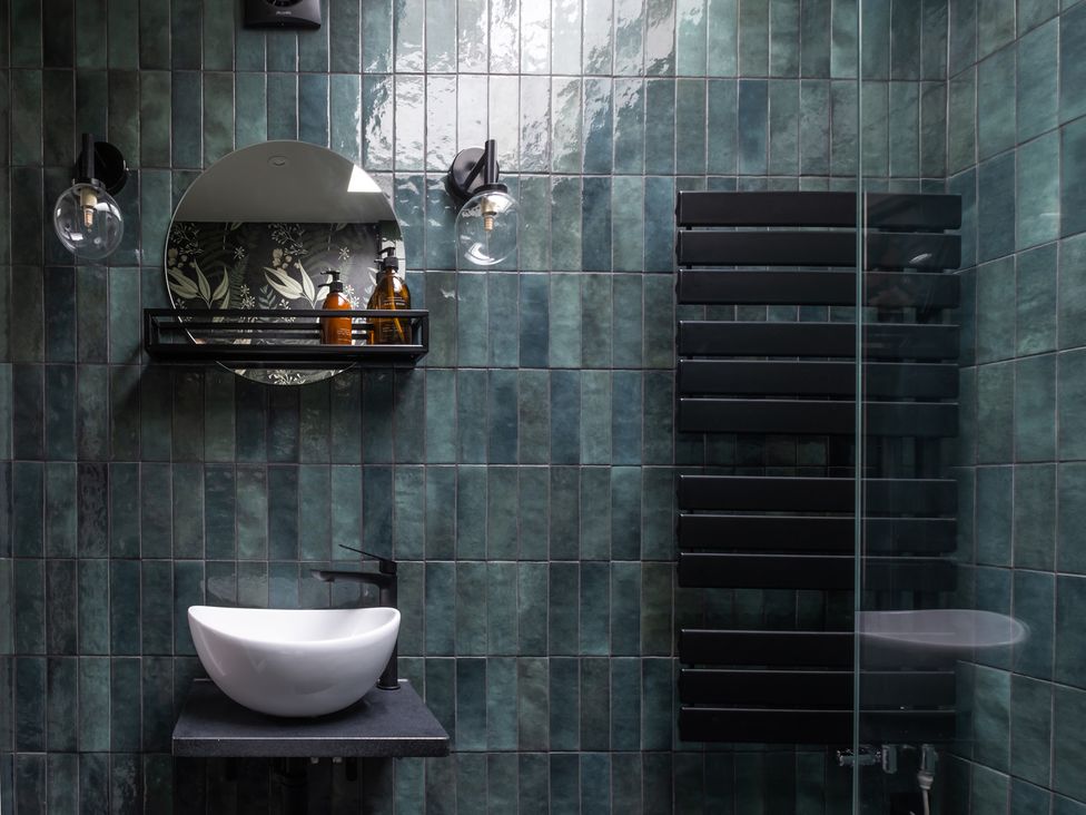 A bathroom with a sink, mirror, shelf, and towel radiator at Honeysuckle Lodge in Knaresborough