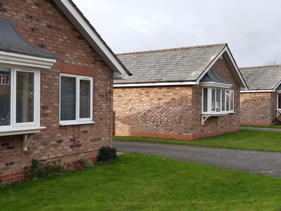 An outdoor view of brick houses with grass and a pathway at 19 Carnaby Mews in Bridlington