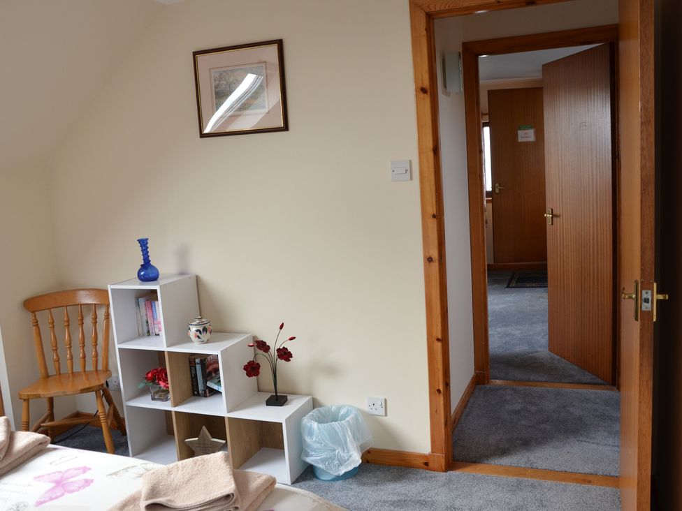 A bedroom with a chair and shelf containing books and a vase at Oran Na Mara Achnasheen