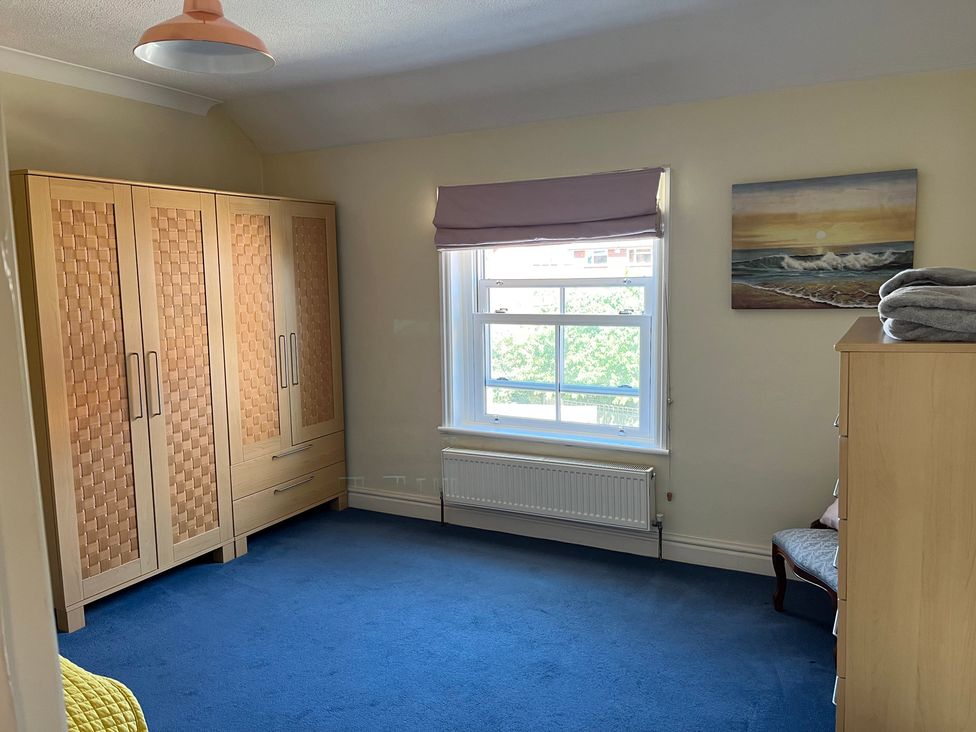 A bedroom with a wardrobe and window at Edal Court in Sheringham