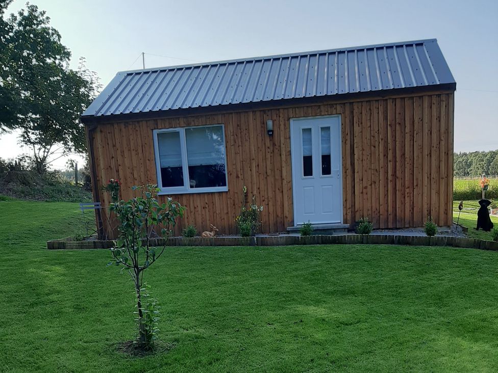 A wooden cabin with a metal roof and plants in the garden at Taigh Nam Moireach in Inverness