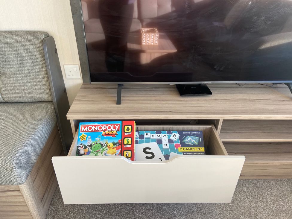 A living room with a television and a drawer containing board games at Elms 32 in Porthcawl