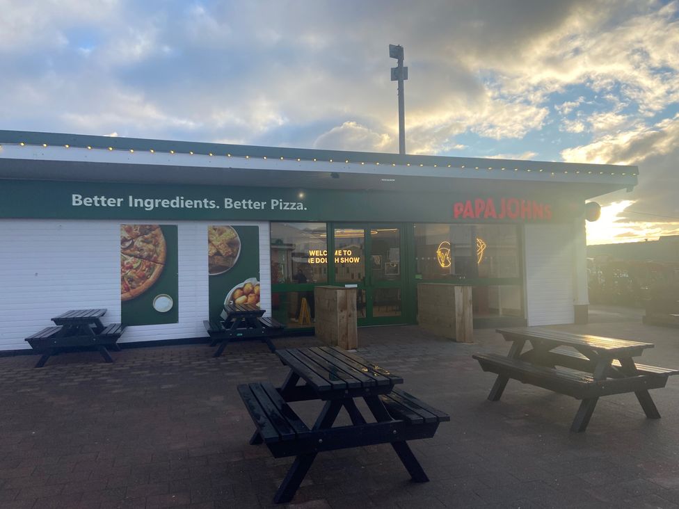 An outdoor area with tables and signage at Papa John's in Porthcawl