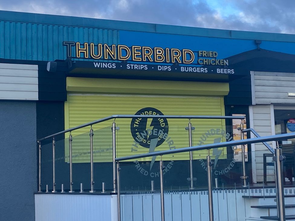 A restaurant sign for Thunderbird Fried Chicken with menu items at Thunderbird in Porthcawl