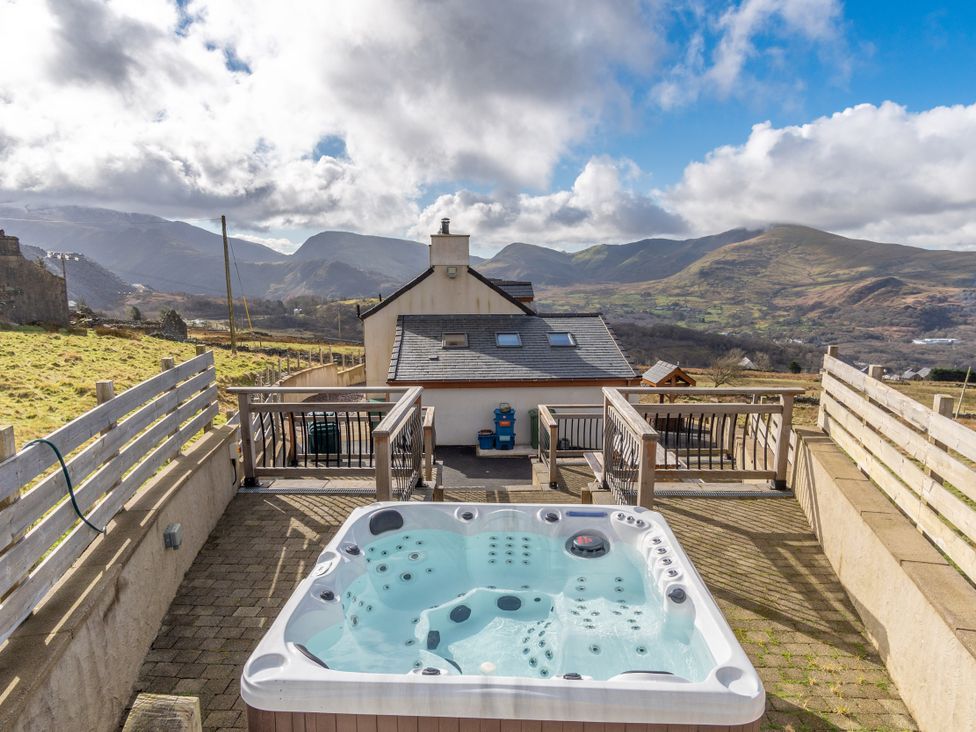 An outdoor area with a hot tub and mountain views at Groeslon Uchaf in Caernarfon