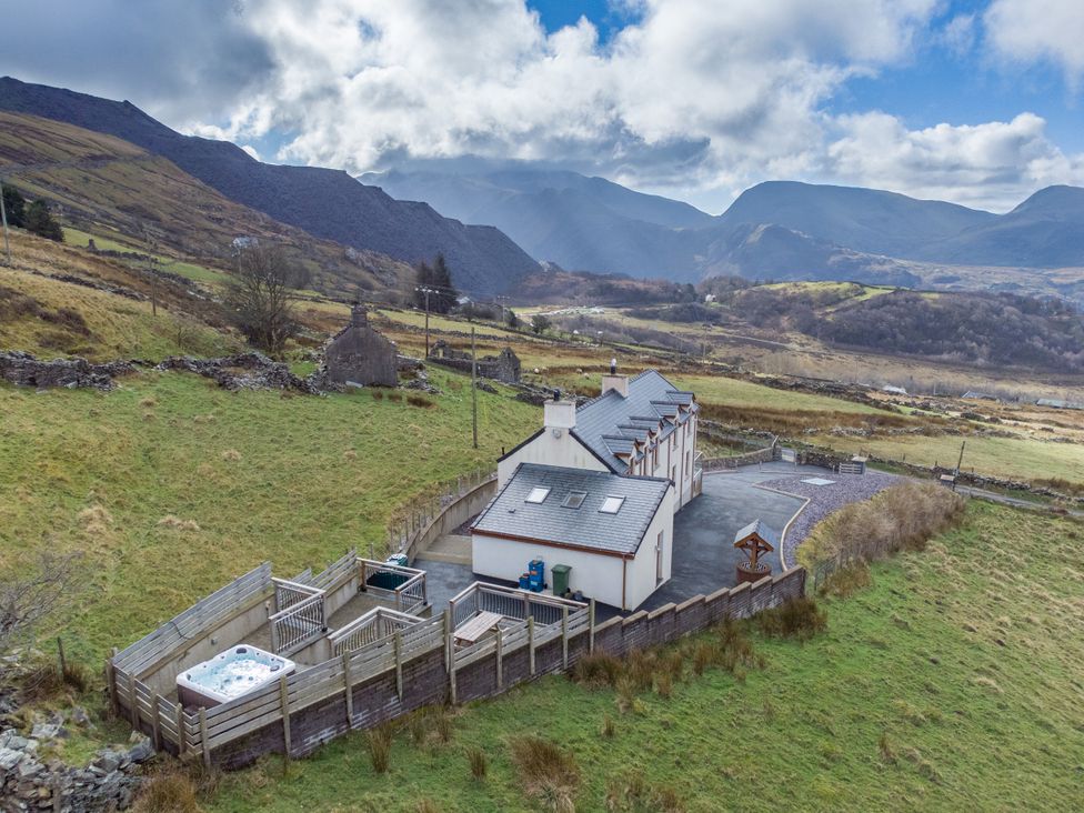 An outdoor view of a house with a hot tub and mountain backdrop at Groeslon Uchaf in Caernarfon