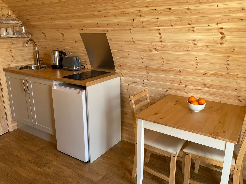 A kitchen area with sink, kettle, toaster, induction hob and a table with oranges at Kirkapol Beach Pod - Flow Isle of Tiree