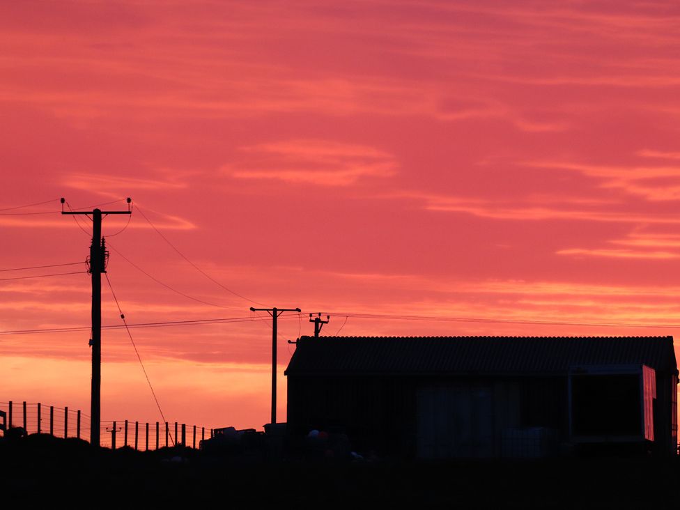 A silhouette of a shed and electric poles against a colorful sky at Kirkapol Beach Pod - Flow Isle of Tiree