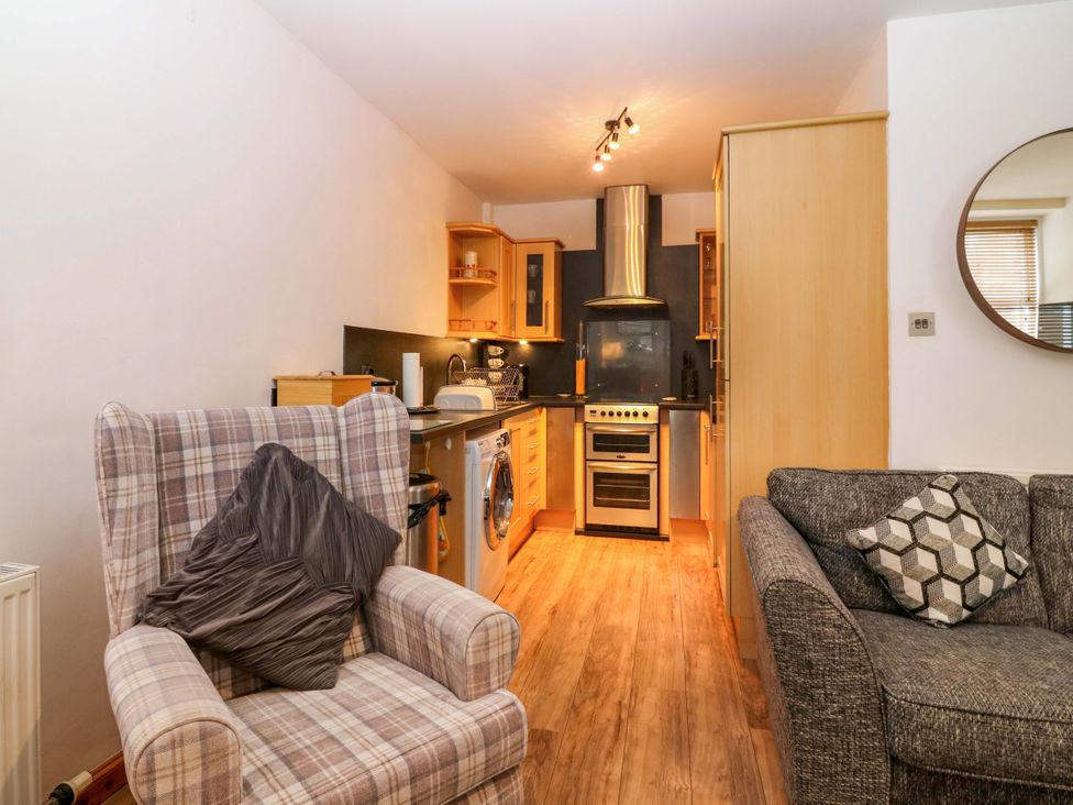 A living room with an armchair and kitchen area at Rose Cottage Nairn