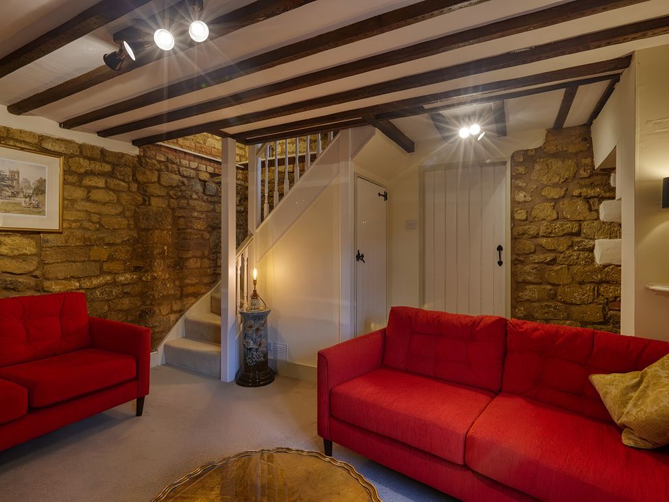 A living room with a staircase and two red sofas at Evas Cottage Southam
