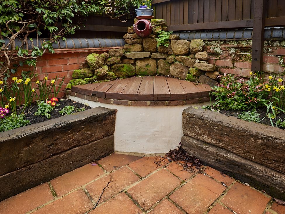 A garden with a wooden platform and flower beds at Evas Cottage in Southam
