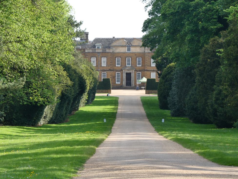 A house viewed from a pathway with trees on the sides at Evas Cottage Southam