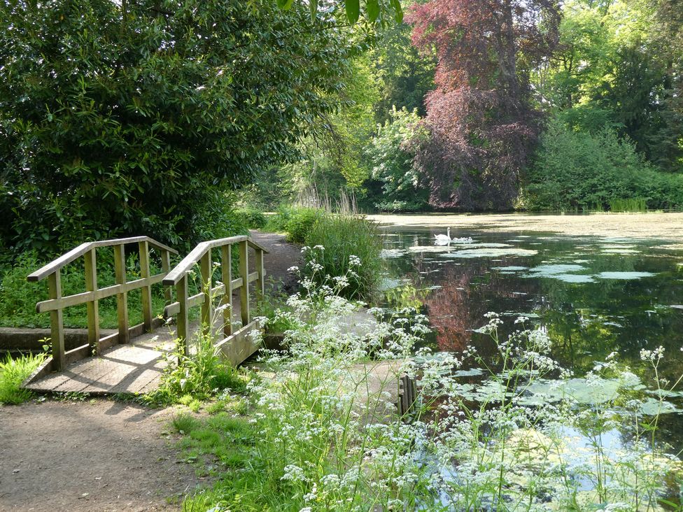 A bridge over water with trees and grass at Evas Cottage Southam