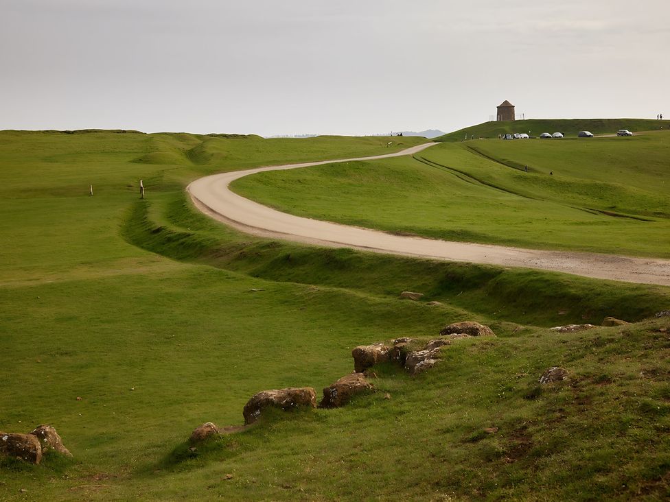 A road winding through grassy hills with a small building at Evas Cottage Southam