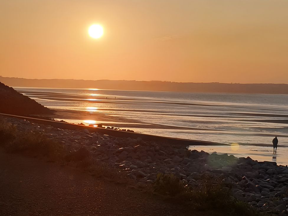 A sunset over the sea with a person walking on the beach at Blue Haven in Penmaenmawr