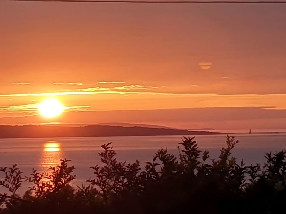 A sunset over the ocean with clouds and an island in the distance at Blue Haven Penmaenmawr