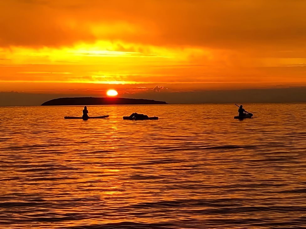 A sunset over the ocean with kayakers at Blue Haven in Penmaenmawr