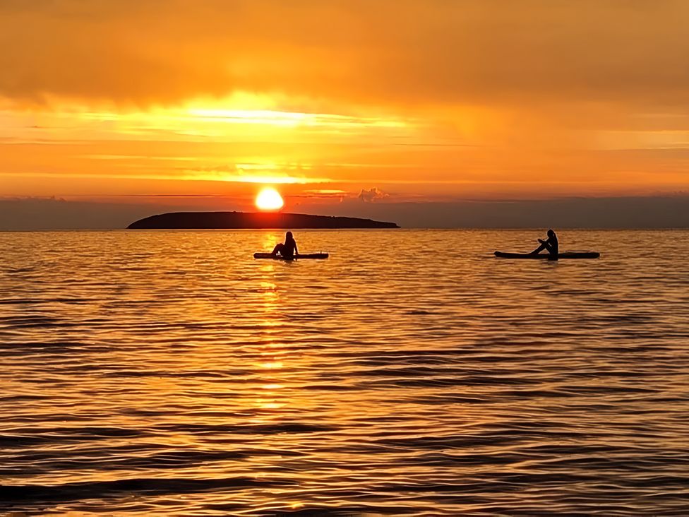 Two people kayaking on water during sunset with an island in the background at Blue Haven in Penmaenmawr