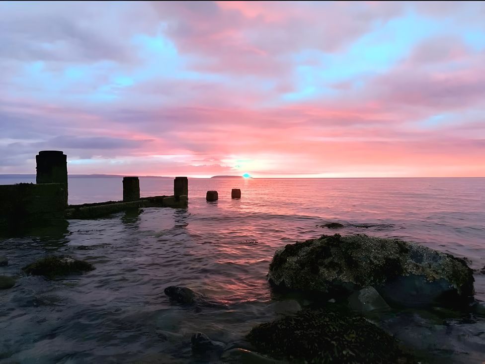 A sunset over water with concrete pillars and rocks at Blue Haven in Penmaenmawr