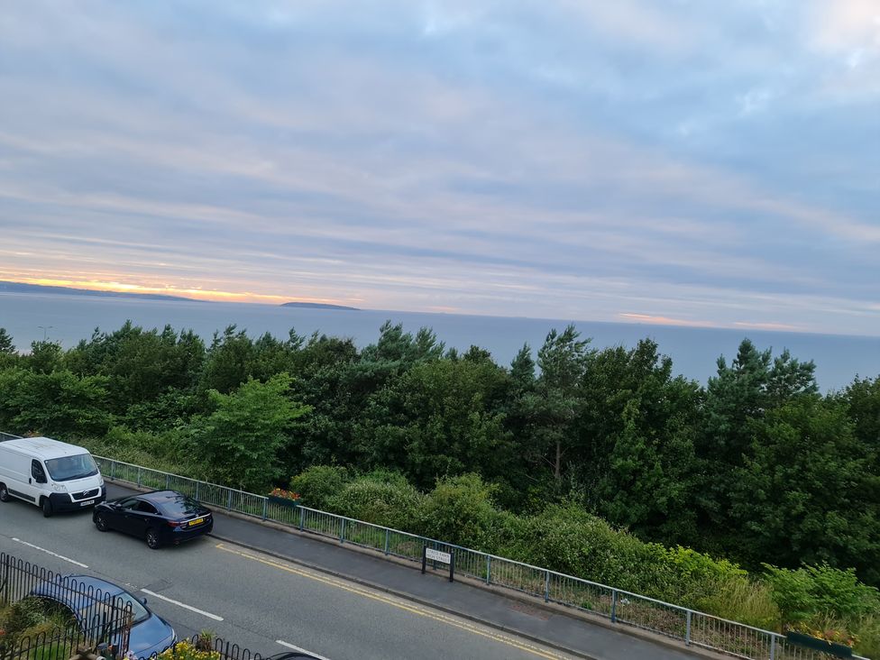 A view of a road with vehicles and trees overlooking the ocean at Sea View Escape in Penmaenmawr