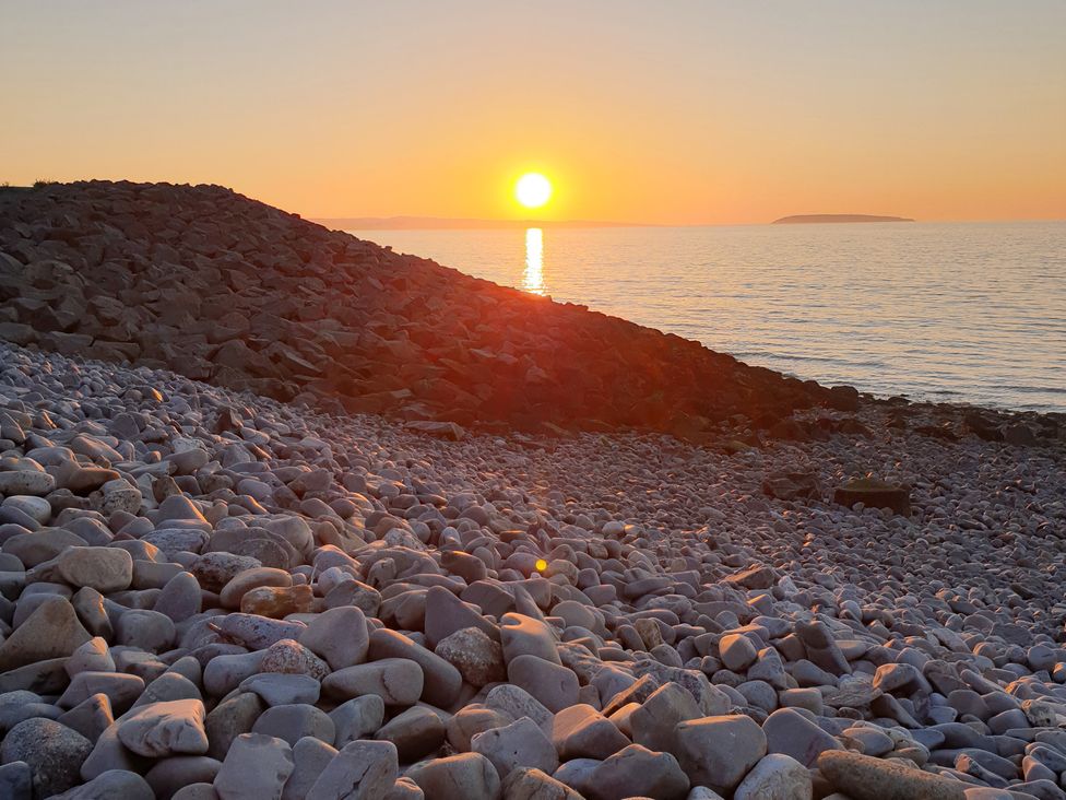 A sunset over the sea with stones on the shore at Sea View Escape in Penmaenmawr