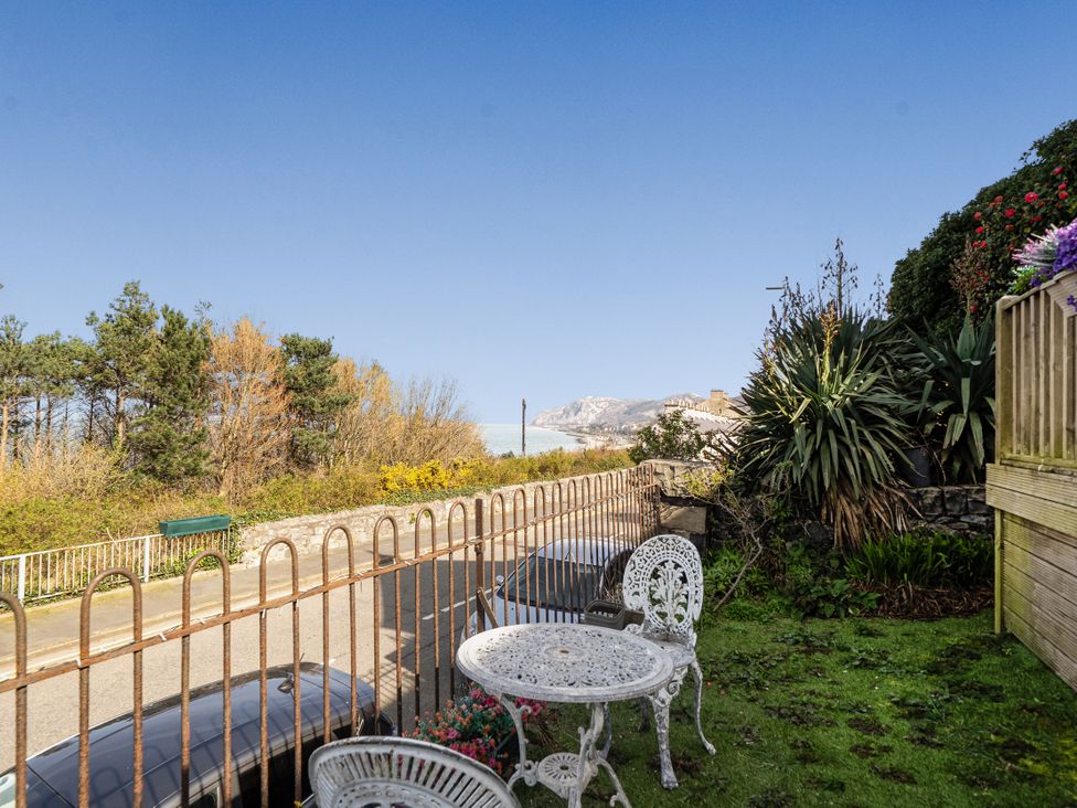 A garden with a table and chair overlooking a road at Sea View Escape in Penmaenmawr