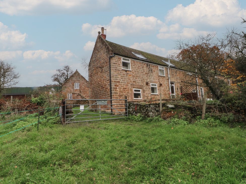 A stone house with a fence and gate surrounded by grass at Meadow View Cottage in Matlock