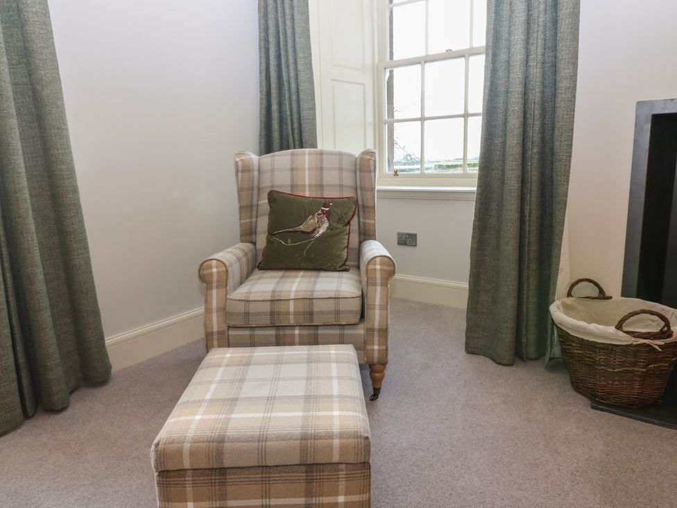 A sitting room with an armchair and an ottoman at Balmashanner Farmhouse in Forfar