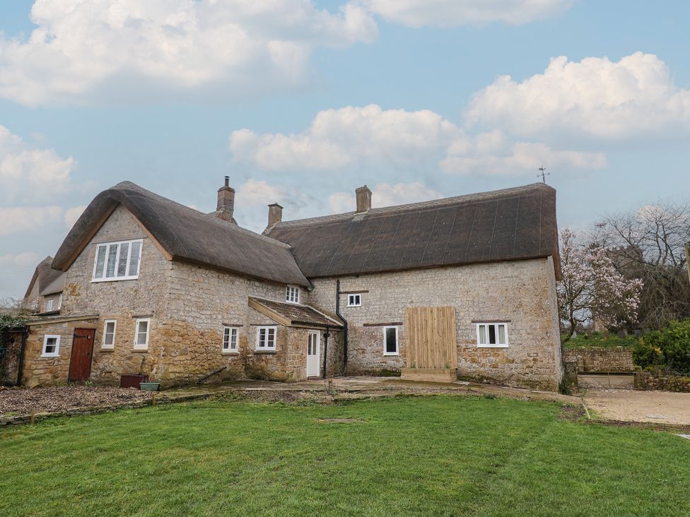 An outdoor view of a stone building with a thatched roof at Manor Cottage in Kingstone near Ilminster