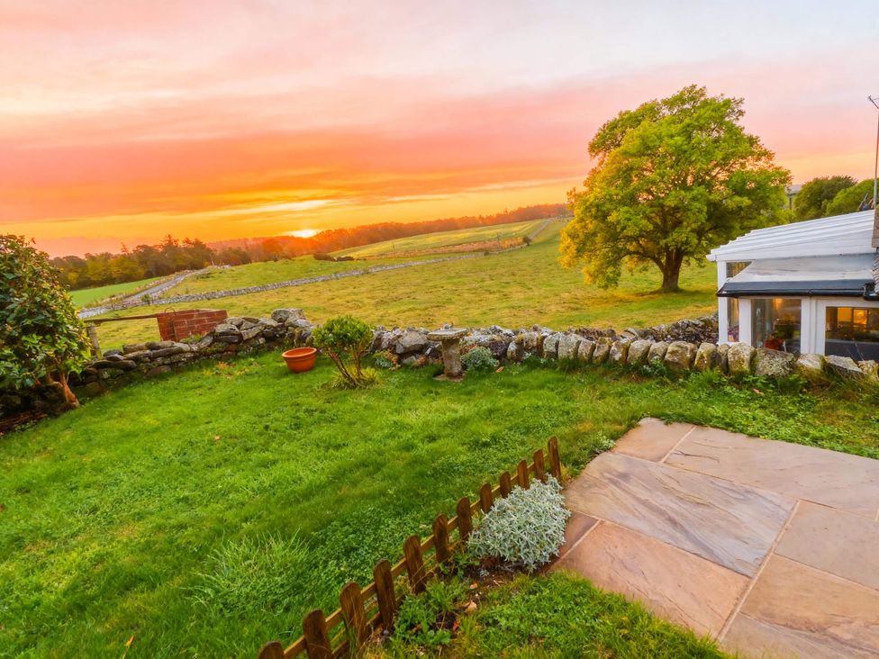 A garden with a stone wall and patio during sunset at 1 Sunny Brae Embleton