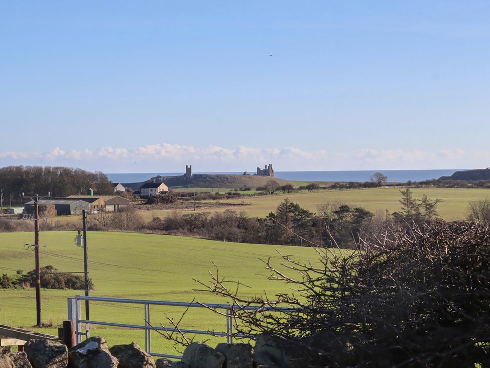 A view of fields and a castle by the sea at Harry's Cottage in Embleton