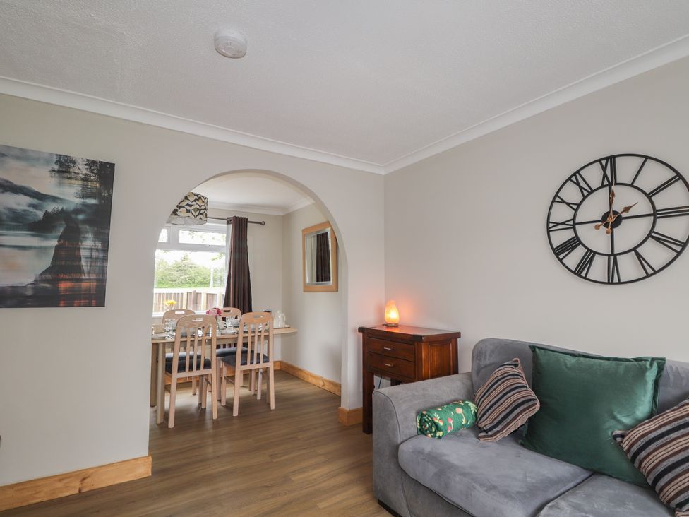 A living room with a clock on the wall and a view to a dining area at Clans Crescent in Nairn