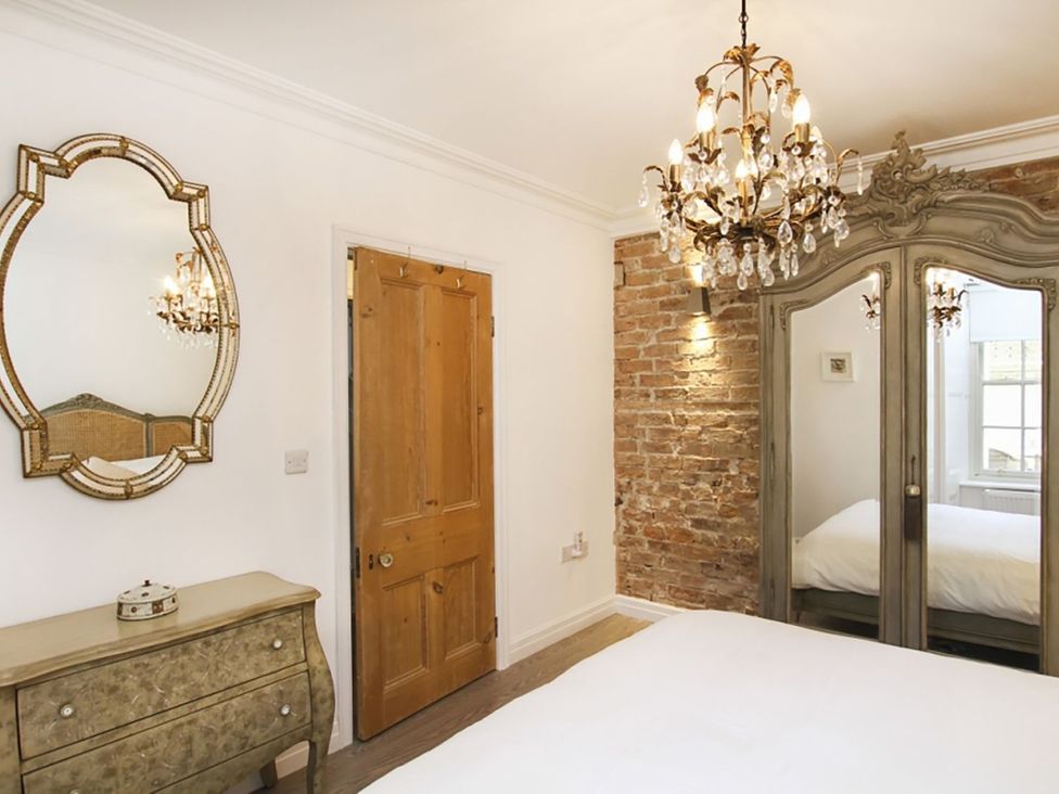 A bedroom with a chandelier and wardrobe at Tri Raglan Bach in Beaumaris
