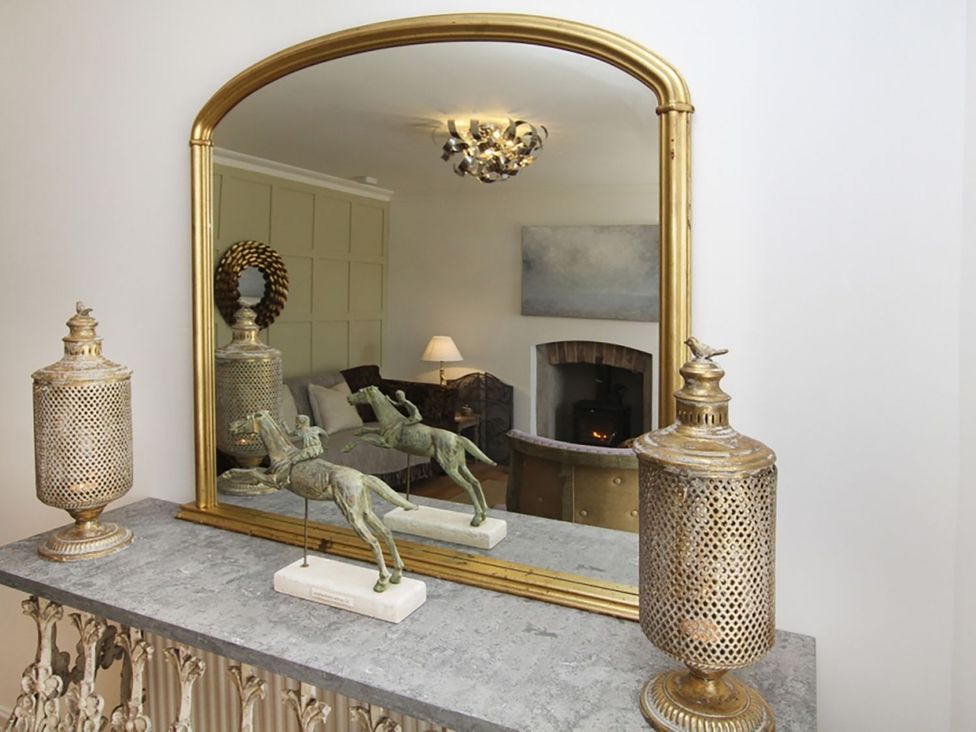 A living room with a mirror and decorative objects at Tri Raglan Bach in Beaumaris