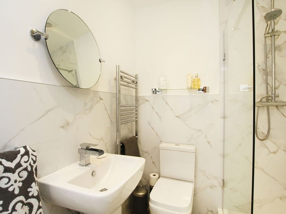 A bathroom with a wash basin, mirror, and a shower at Tri Raglan Bach in Beaumaris