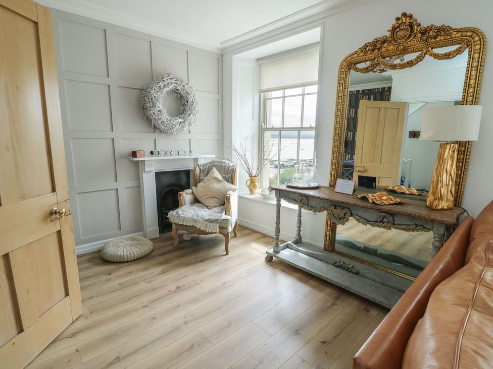 A living room with a chair and a mirror at Tri Raglan Mawr in Beaumaris