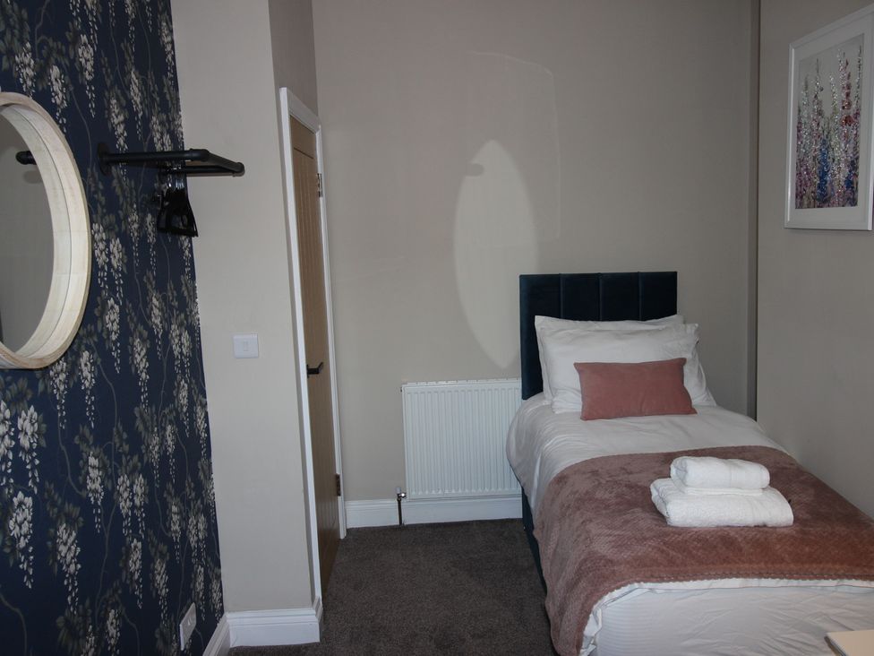 A bedroom with a single bed and a mirror at Blackburn Heights Apartment in Bridlington