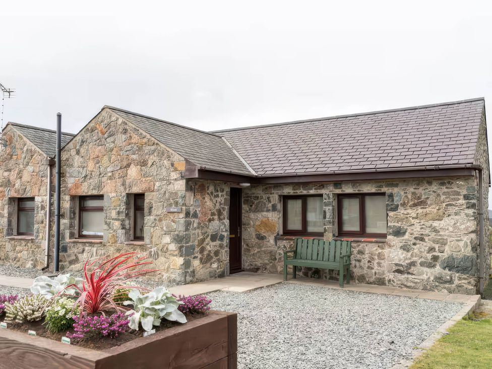 A stone cottage with a green bench and flower bed at Black Bird Cottage in Llangaffo