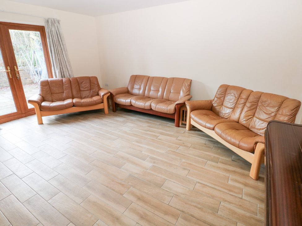 A living room with leather sofas and a glass door at Ty-Gan Dderwen in Llanelli