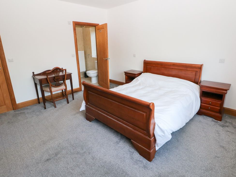 A bedroom with a bed, nightstand, table, and chair at Ty-Gan Dderwen in Llanelli