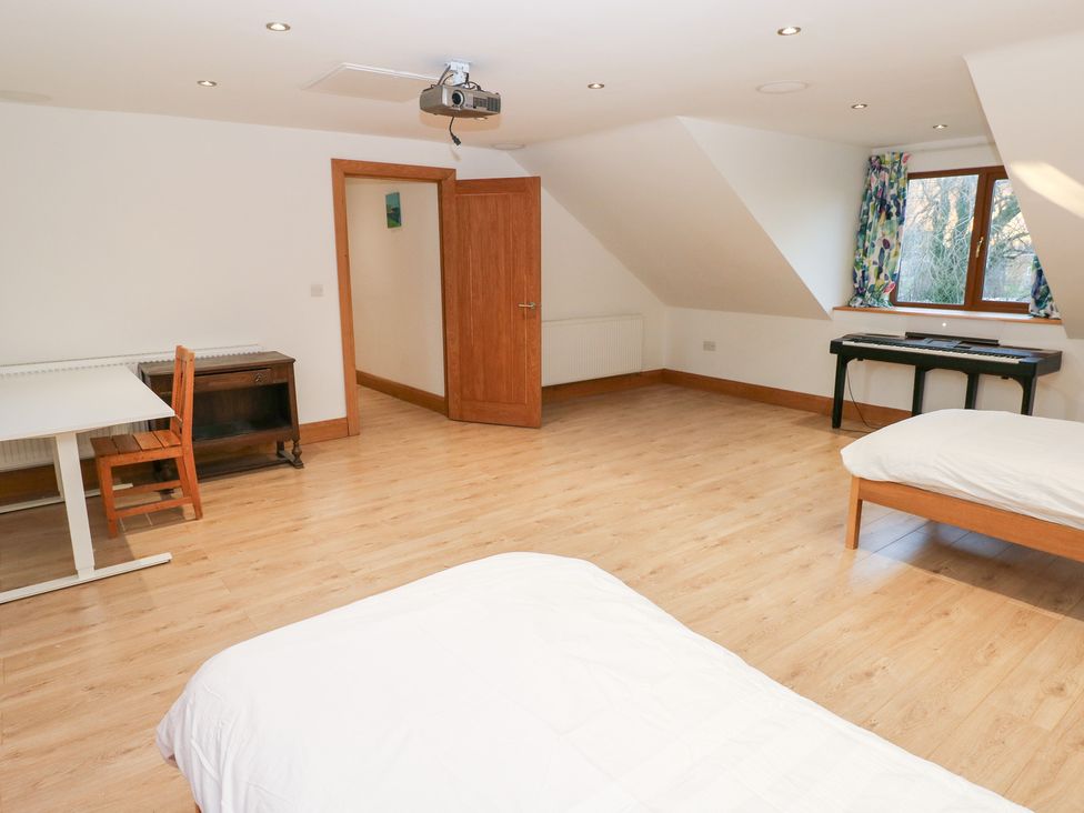 A bedroom with two beds, a table, a chair, a projector, and a keyboard at Ty-Gan Dderwen in Llanelli