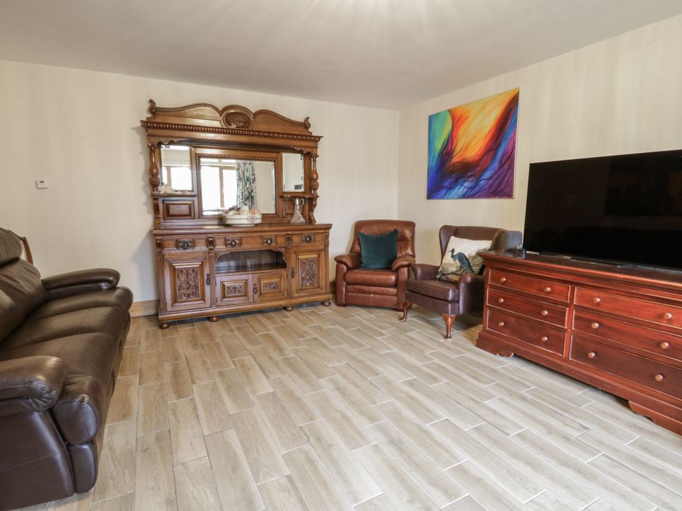 A living room with a sofa, armchair, cabinets, and television at Ty-Gan Dderwen in Llangennech